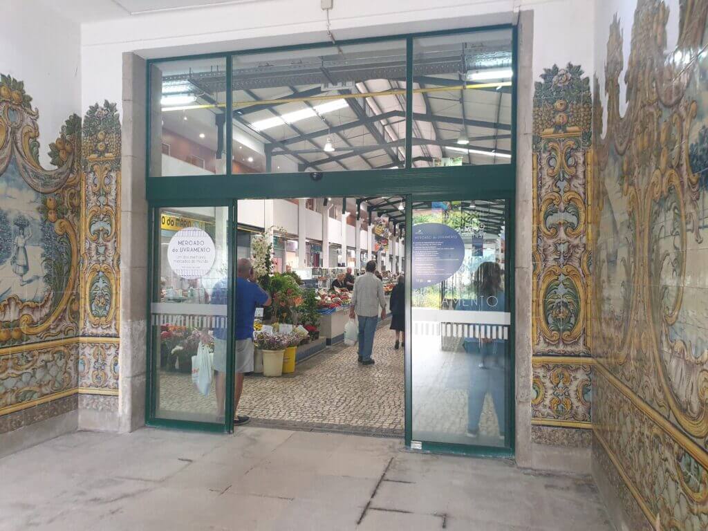 A glass door entrance to the Market follows a faded yet exquisite wall mural showing people carrying baskets amid orange and grape bunches in a rural setting.