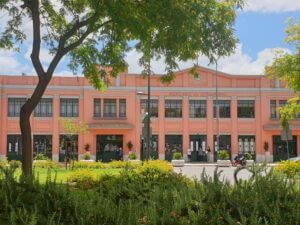 The loud pink and dark green facade of the Livramento Market building pops against a western blue sky. It's seen from Luisa Todi Avenue in Setúbal.