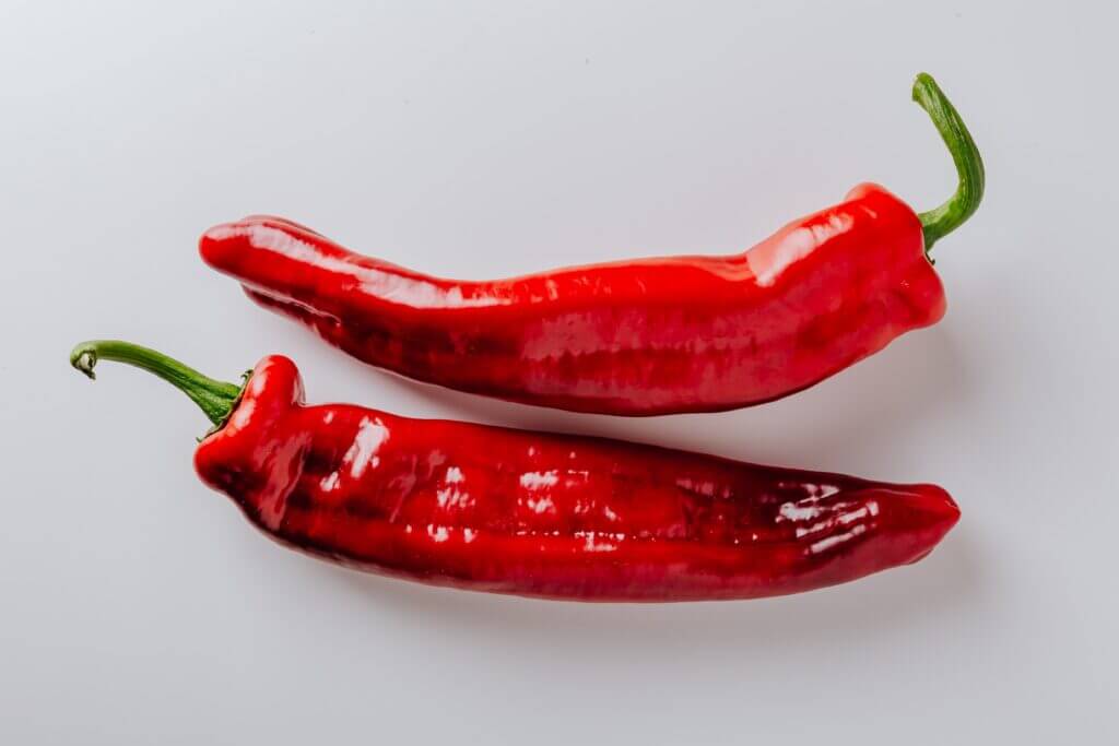 Two red chilli pepper lie side-by-side on a white background